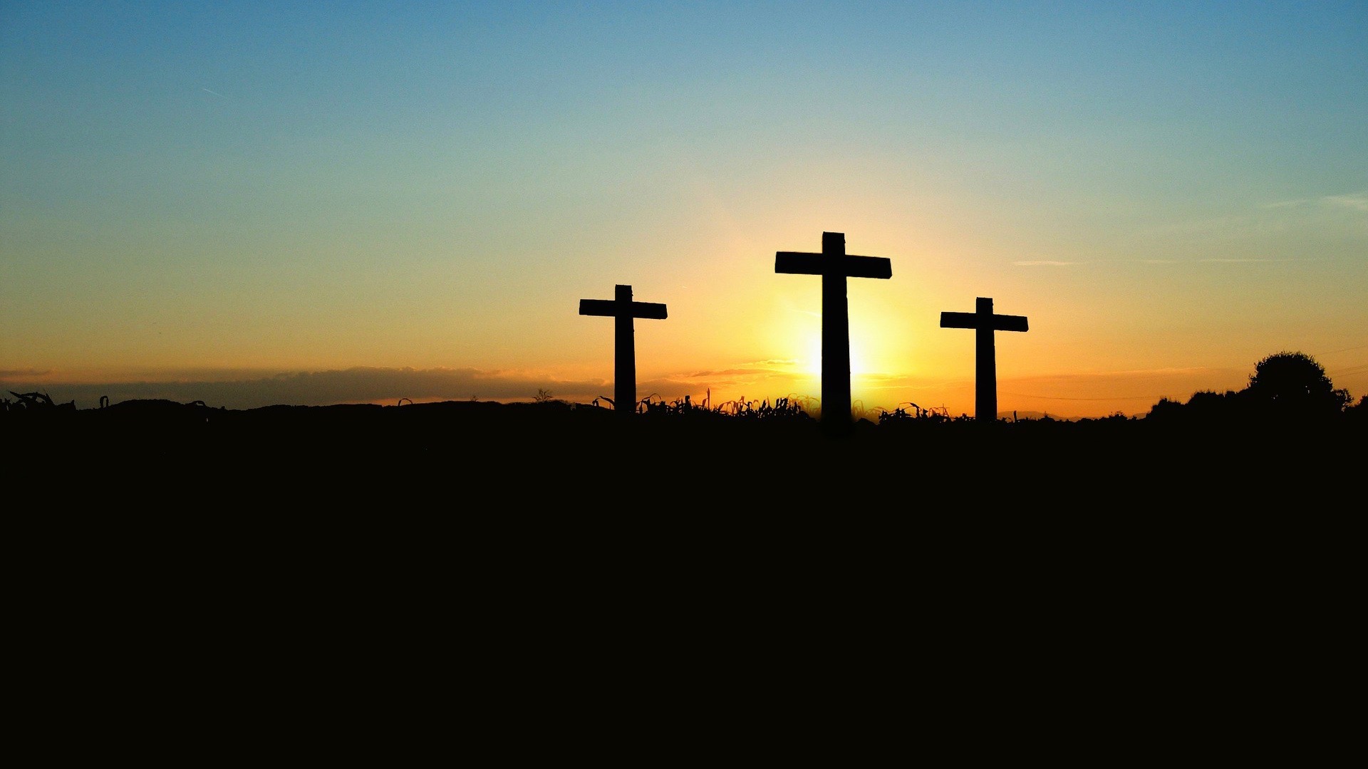 Three crosses in silhouette in front of a yellow sunset.